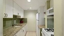 kitchen featuring sink, light tile patterned flooring, white appliances, white cabinetry, and light stone countertops