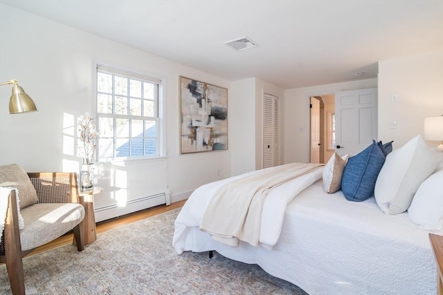 bedroom featuring wood-type flooring, a baseboard radiator, and a closet