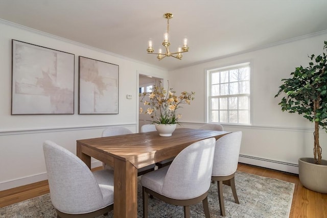 dining area with baseboard heating, crown molding, light wood-type flooring, and an inviting chandelier