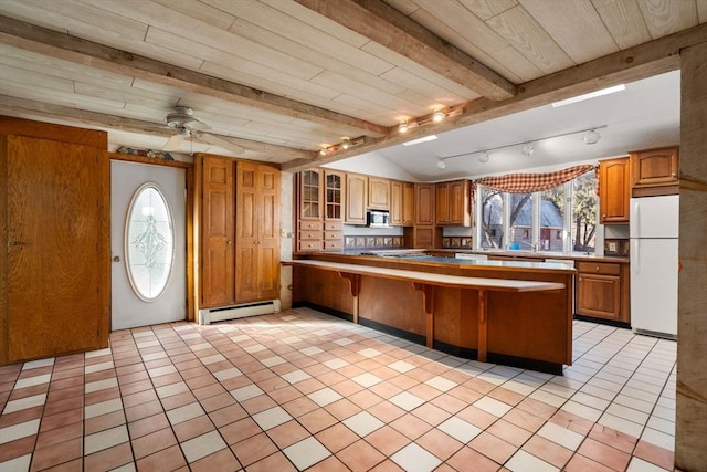 kitchen with stainless steel microwave, a baseboard heating unit, a kitchen breakfast bar, freestanding refrigerator, and brown cabinetry