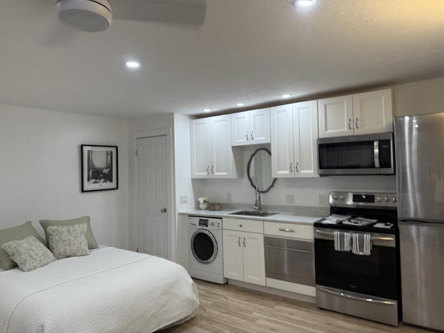 kitchen featuring stainless steel appliances, washer / clothes dryer, light wood-style flooring, white cabinetry, and a sink