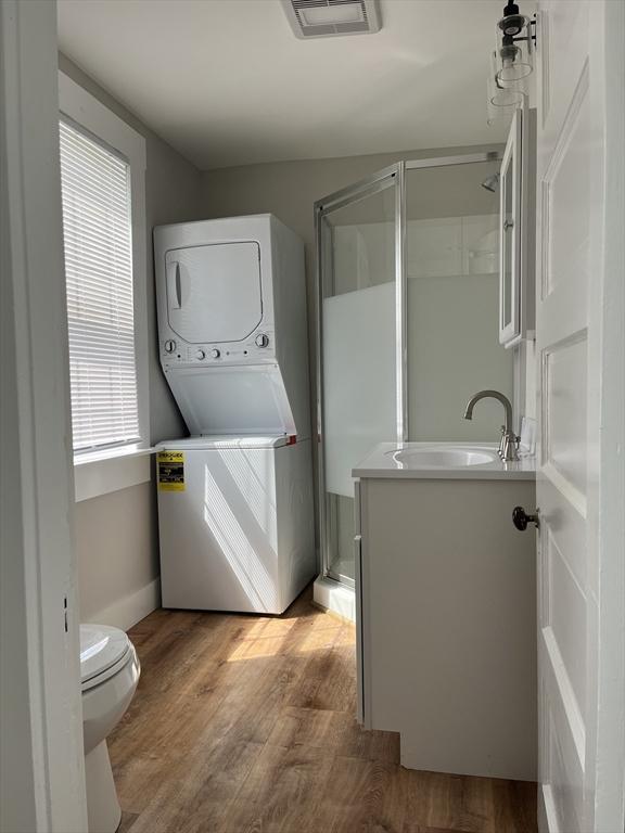 clothes washing area featuring stacked washer / dryer, sink, and light hardwood / wood-style floors