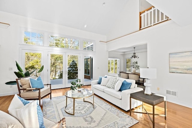 living room with french doors, a chandelier, high vaulted ceiling, and light wood-type flooring