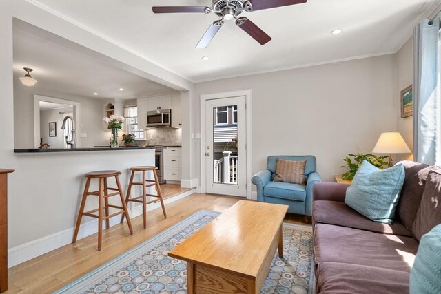 living area with ornamental molding, baseboards, ceiling fan, recessed lighting, and light wood finished floors