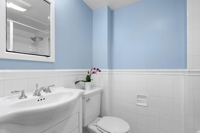 bathroom featuring walk in shower, vanity, toilet, a wainscoted wall, and tile walls