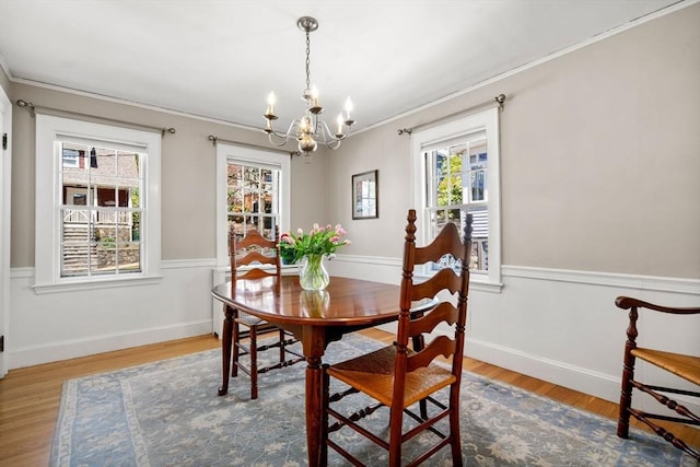 dining area featuring an inviting chandelier, ornamental molding, wainscoting, and wood finished floors