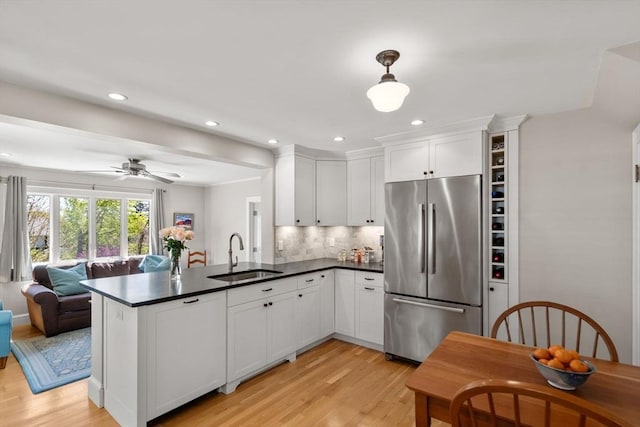 kitchen featuring dark countertops, a sink, open floor plan, stainless steel fridge, and light wood-style flooring