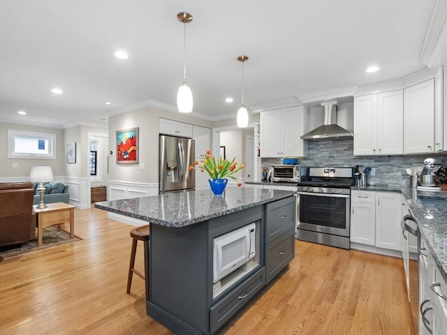 83 Boynton St, Waltham, MA 02453 - kitchen featuring stainless steel appliances, wall chimney range hood, crown molding, white cabinets, and a kitchen island