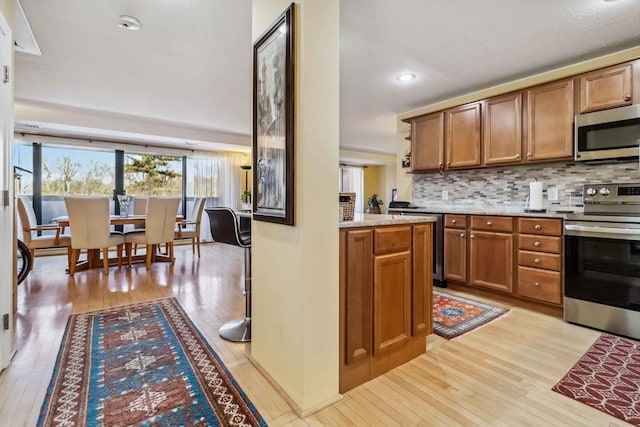 kitchen featuring brown cabinets, light wood-type flooring, tasteful backsplash, and stainless steel appliances