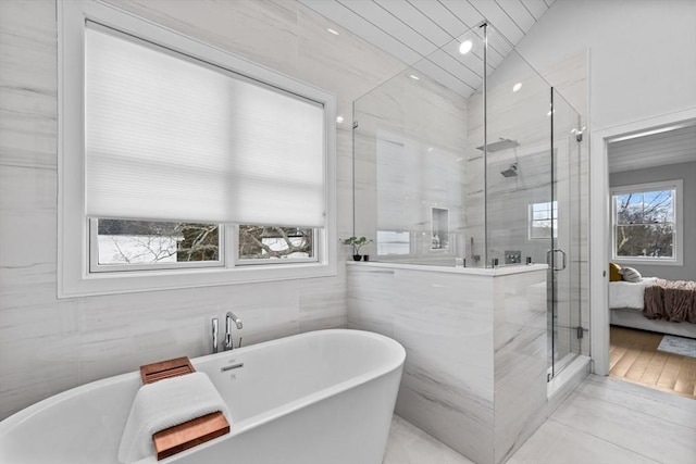 ensuite bathroom with ensuite bathroom, tile walls, a freestanding bath, vaulted ceiling, and a stall shower