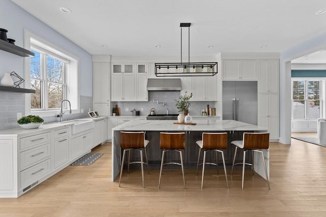 kitchen featuring open shelves, white cabinetry, a sink, light wood-type flooring, and under cabinet range hood