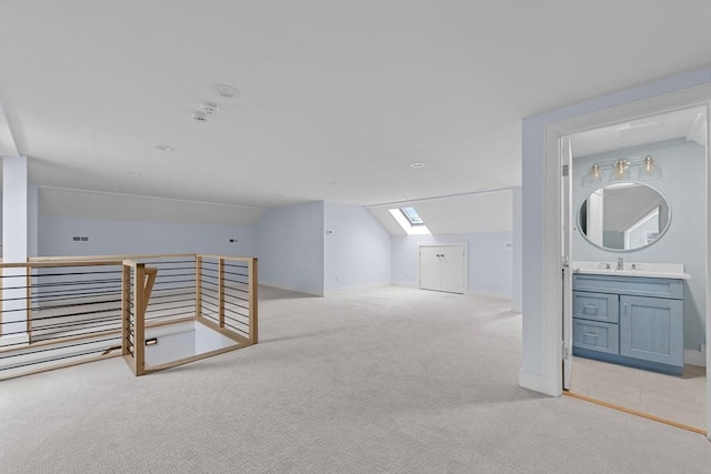 additional living space featuring lofted ceiling with skylight, baseboards, a sink, and light colored carpet