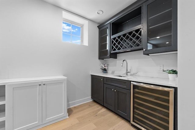 bar with light wood finished floors, baseboards, wine cooler, indoor wet bar, and a sink