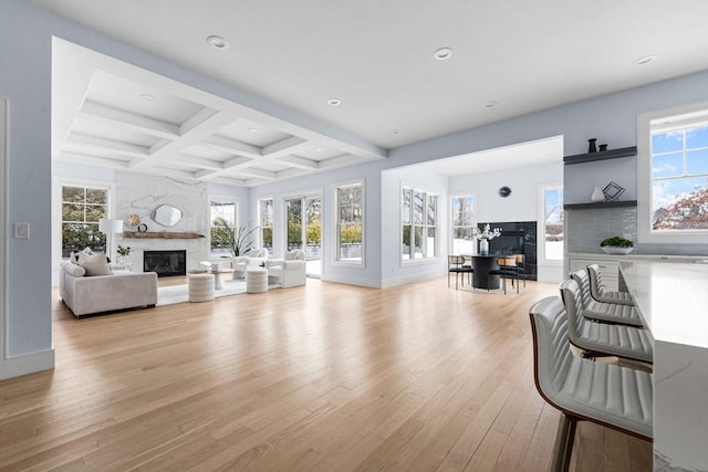 living area with a large fireplace, plenty of natural light, coffered ceiling, light wood-style flooring, and beamed ceiling