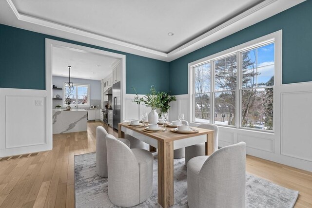 dining room featuring a raised ceiling, a wainscoted wall, a decorative wall, and light wood-style flooring