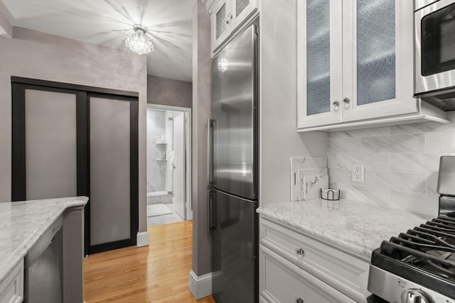 42 8th St Unit 4106, Boston, MA 02129 - kitchen with stainless steel appliances, light wood-style flooring, white cabinetry, light stone counters, and decorative backsplash