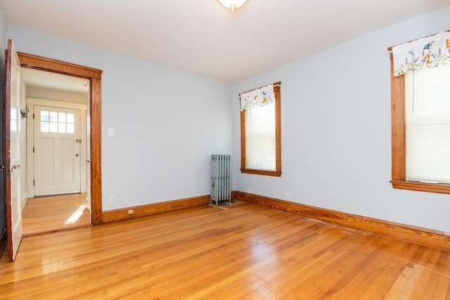 unfurnished room with light wood-style floors, radiator, and baseboards