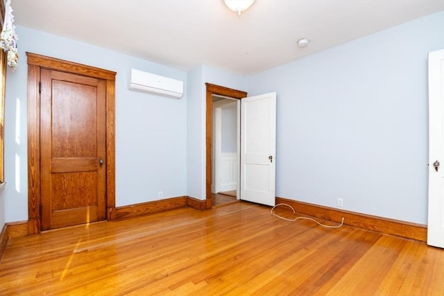 unfurnished bedroom featuring a wall unit AC, light wood-style flooring, and baseboards