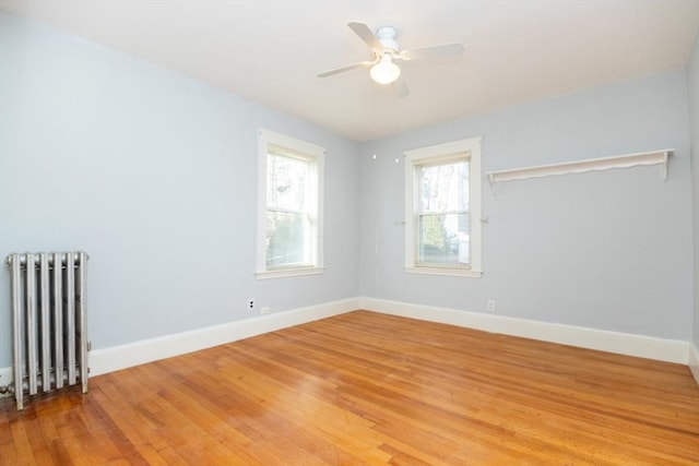 empty room with a ceiling fan, radiator heating unit, baseboards, and wood finished floors