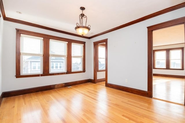 empty room featuring baseboards, crown molding, and light wood finished floors