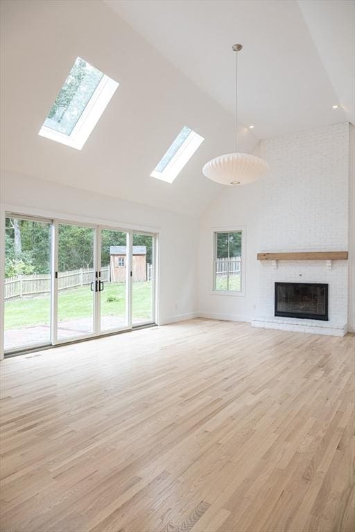 unfurnished living room with a healthy amount of sunlight, light wood-type flooring, high vaulted ceiling, and a brick fireplace