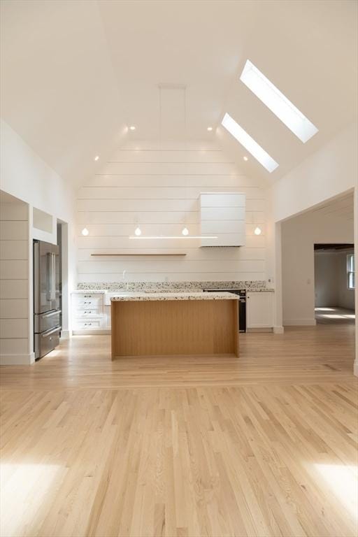 kitchen featuring light stone countertops, a center island, light hardwood / wood-style flooring, high vaulted ceiling, and stainless steel fridge