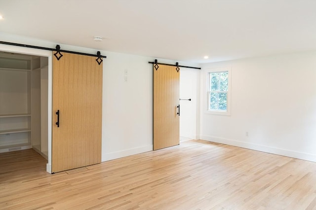 unfurnished room with a barn door and light hardwood / wood-style floors