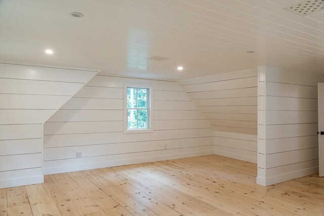 bonus room with light wood-type flooring, wooden walls, and vaulted ceiling