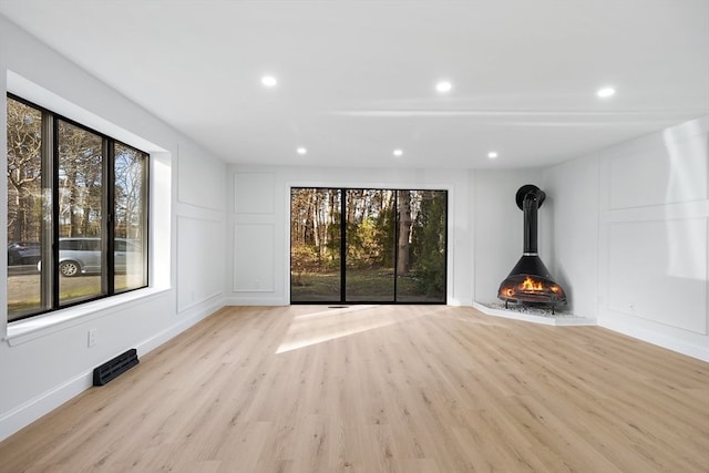 unfurnished living room featuring a wood stove, plenty of natural light, and light hardwood / wood-style flooring