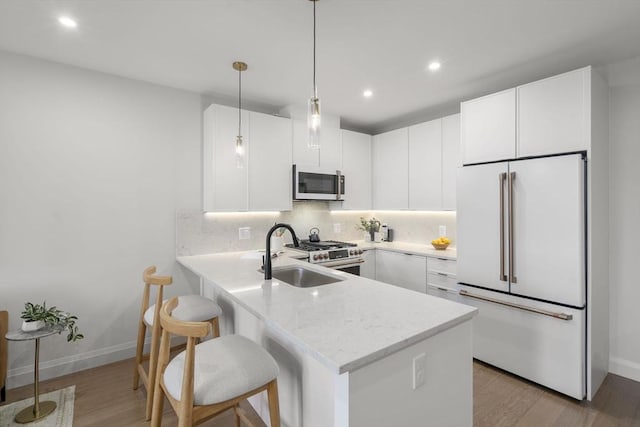 100 Lincoln St Unit 303, Boston, MA 02135 - kitchen featuring high end appliances, light wood-type flooring, a peninsula, tasteful backsplash, and white cabinetry