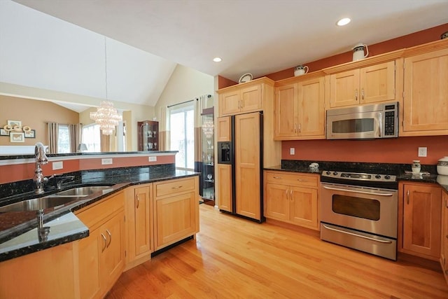 kitchen with appliances with stainless steel finishes, an inviting chandelier, a sink, light wood-style flooring, and vaulted ceiling