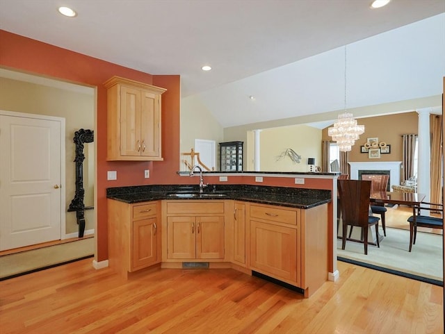 kitchen featuring an inviting chandelier, a sink, light wood finished floors, a peninsula, and decorative light fixtures