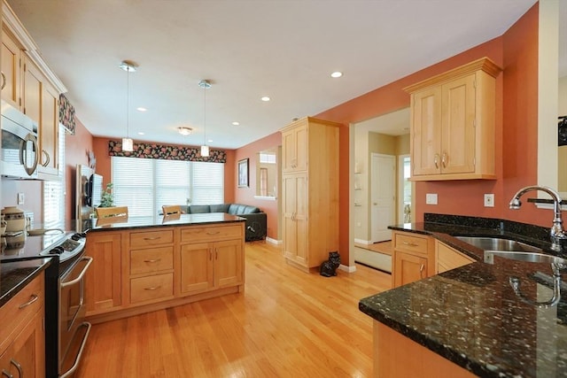 kitchen featuring light wood-type flooring, a sink, appliances with stainless steel finishes, and a peninsula