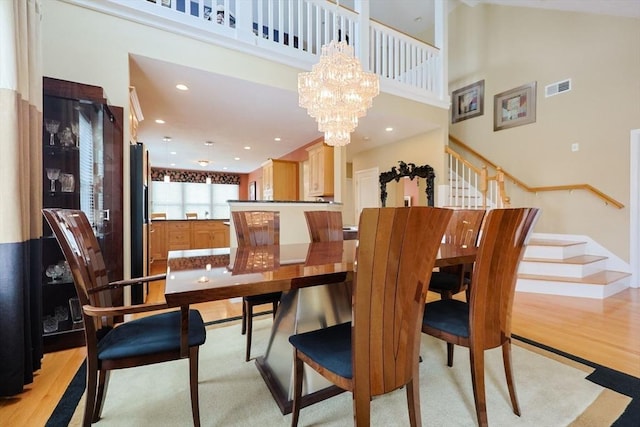 dining room featuring visible vents, an inviting chandelier, stairs, a high ceiling, and light wood finished floors