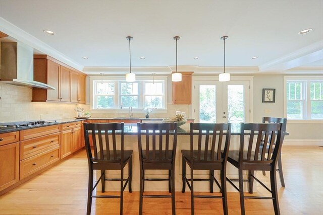 185 Read St, Seekonk, MA 02771 - kitchen featuring wall chimney exhaust hood, gas cooktop, light wood-style flooring, tasteful backsplash, and a breakfast bar