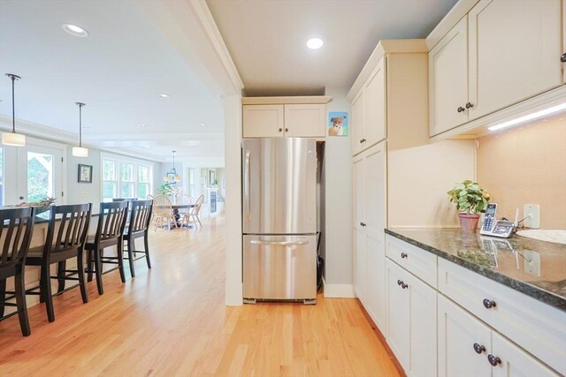 185 Read St, Seekonk, MA 02771 - kitchen with freestanding refrigerator, dark stone counters, light wood-type flooring, white cabinets, and hanging light fixtures