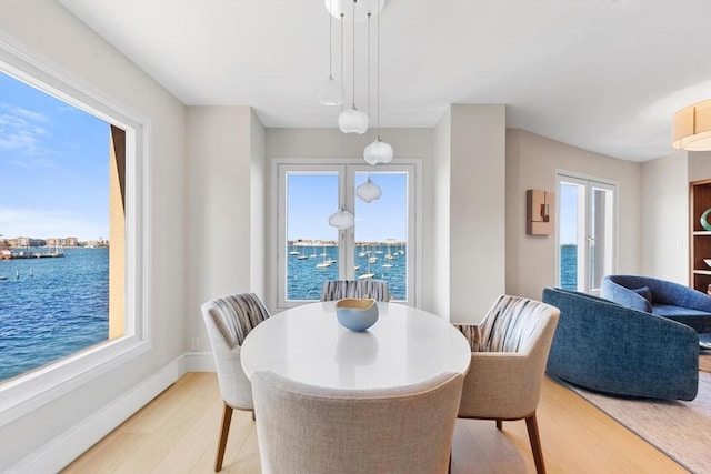 dining room featuring light wood-style floors, a water view, and baseboards