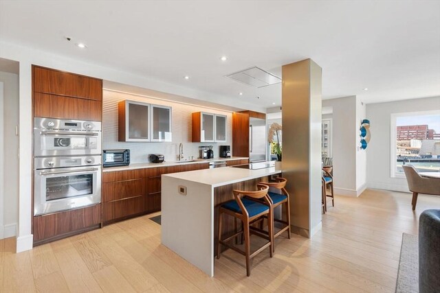 kitchen featuring modern cabinets, light wood-type flooring, a kitchen bar, appliances with stainless steel finishes, and light countertops