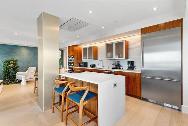 kitchen with appliances with stainless steel finishes, modern cabinets, brown cabinets, light countertops, and light wood finished floors