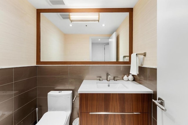 half bathroom with tile walls, toilet, and vanity