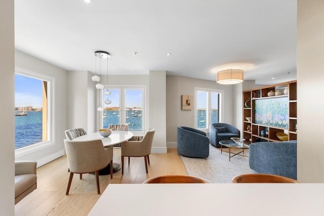 dining room with wood finished floors, a water view, baseboards, and recessed lighting