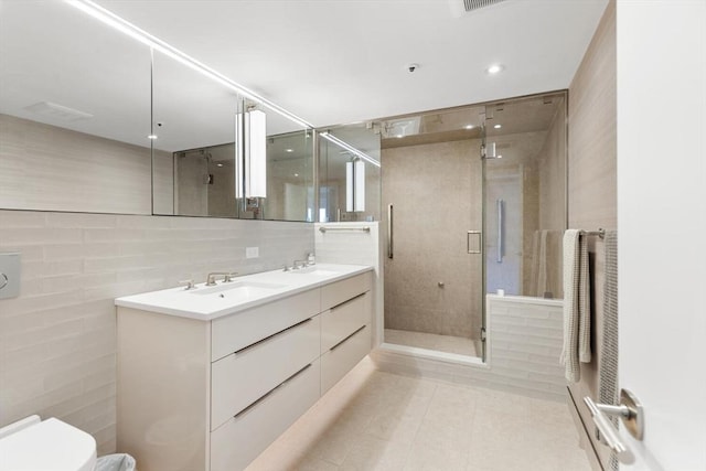 full bath featuring toilet, a shower stall, tile patterned floors, double vanity, and tile walls