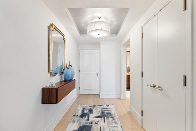 corridor featuring a raised ceiling, light wood-type flooring, and baseboards