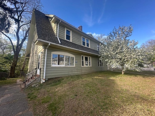 view of side of home featuring a chimney, a yard, and a shingled roof