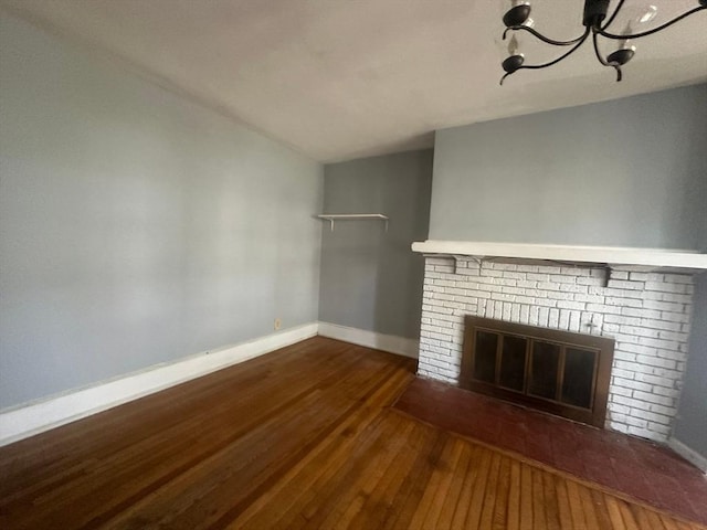 unfurnished living room featuring hardwood / wood-style flooring, a brick fireplace, a chandelier, and baseboards