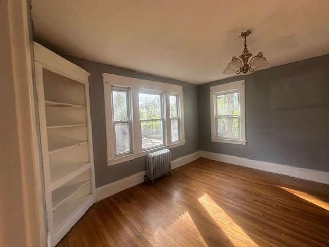 spare room featuring radiator, a chandelier, hardwood / wood-style flooring, and baseboards