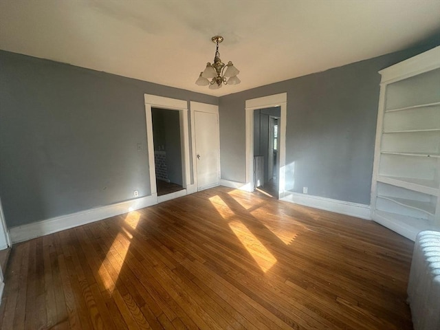 unfurnished room with a chandelier, baseboards, wood-type flooring, and built in features