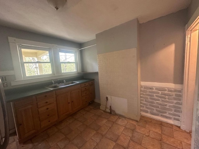 kitchen featuring a sink, dark countertops, light stone finish floors, and brick wall
