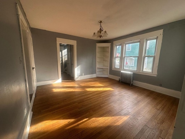 unfurnished dining area featuring radiator, light wood-style flooring, baseboards, a chandelier, and built in shelves