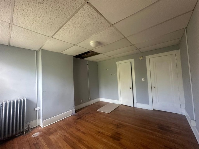 spare room featuring radiator, a paneled ceiling, baseboards, and wood finished floors